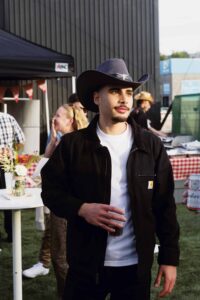 Homme avec chapeau cowboy lors d'un événement en extérieur, ambiance conviviale et décontractée.