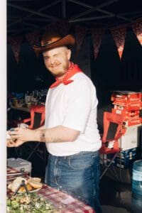 Homme portant un chapeau de cowboy lors d'un événement convivial, avec décorations et stands en arri.