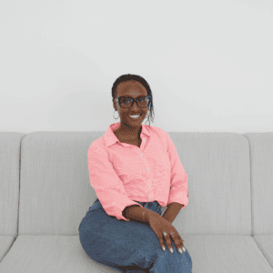 Femme souriante en tenue décontractée assise sur un canapé gris clair.