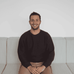 Homme souriant assis sur canapé moderne en tissu beige, intérieur lumineux.