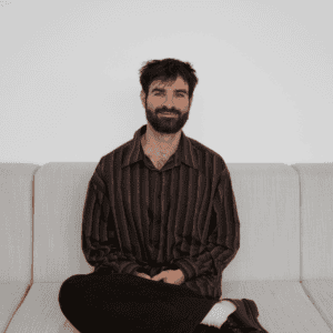 Homme assis sur un canapé gris clair, look décontracté, intérieur moderne.